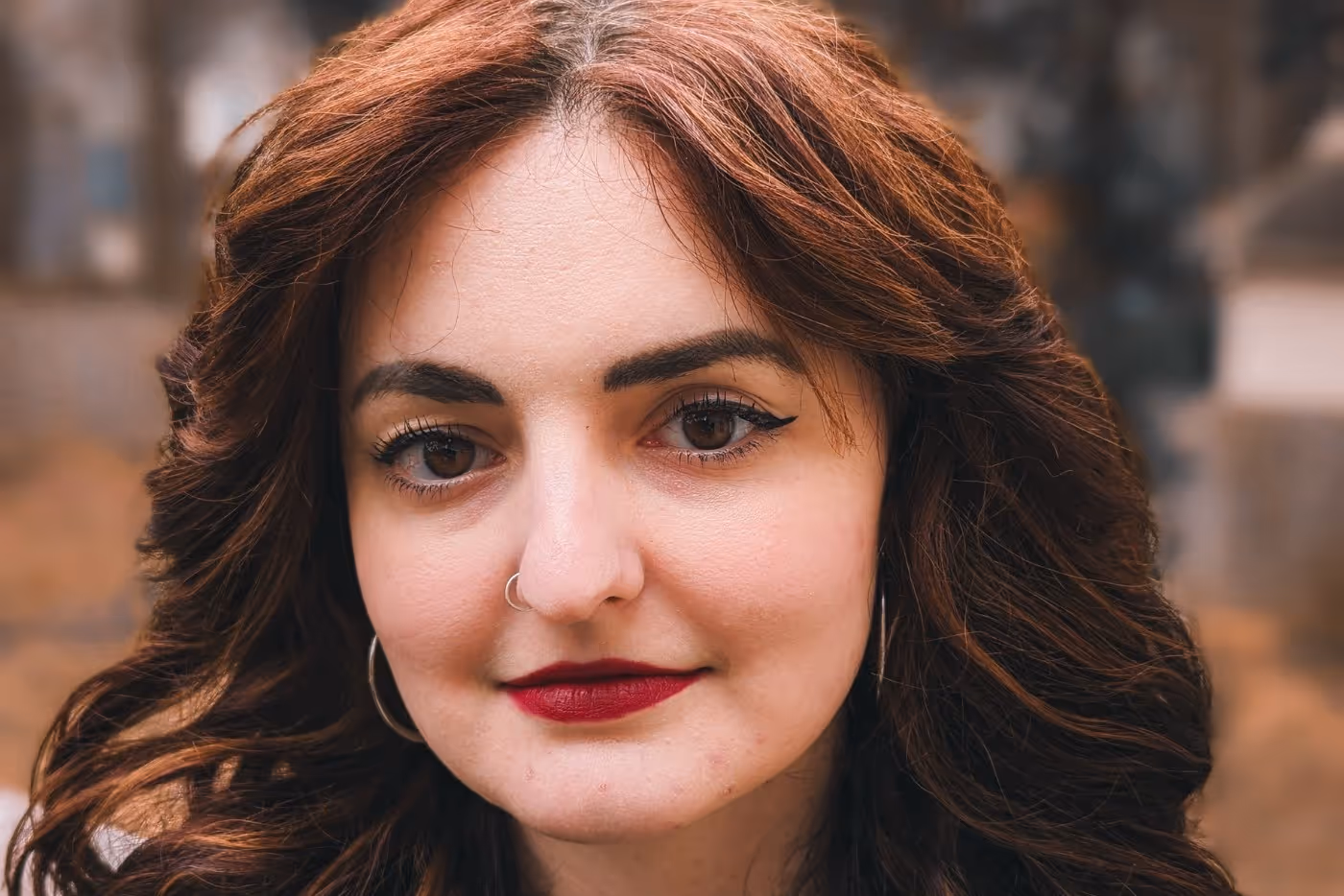 Close-up portrait of Briana Morgan with curled auburn hair, bold eyeliner, and a calm, confident expression.
