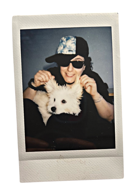 Me playing with my cute dog, I wear a hat and a pair of sunglasses, and I am holding my dog's ears above her head with a forced smile on lmy face