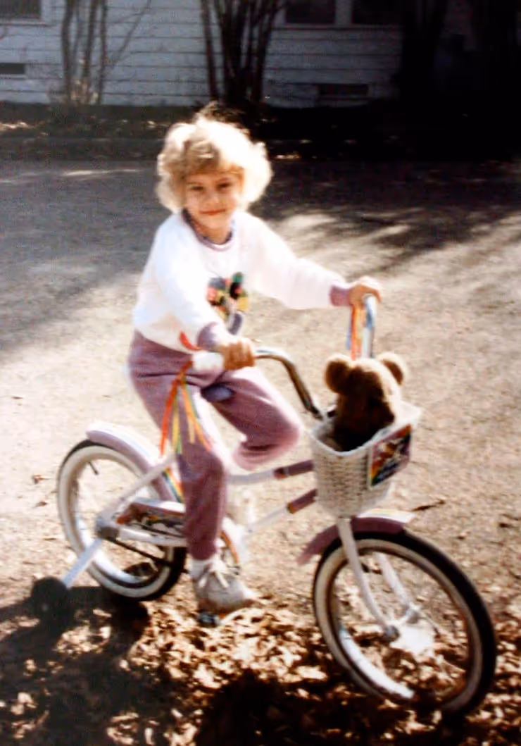 A picture of Kathleen as a child. She is on a bicycle, looking and smiling at the camera.