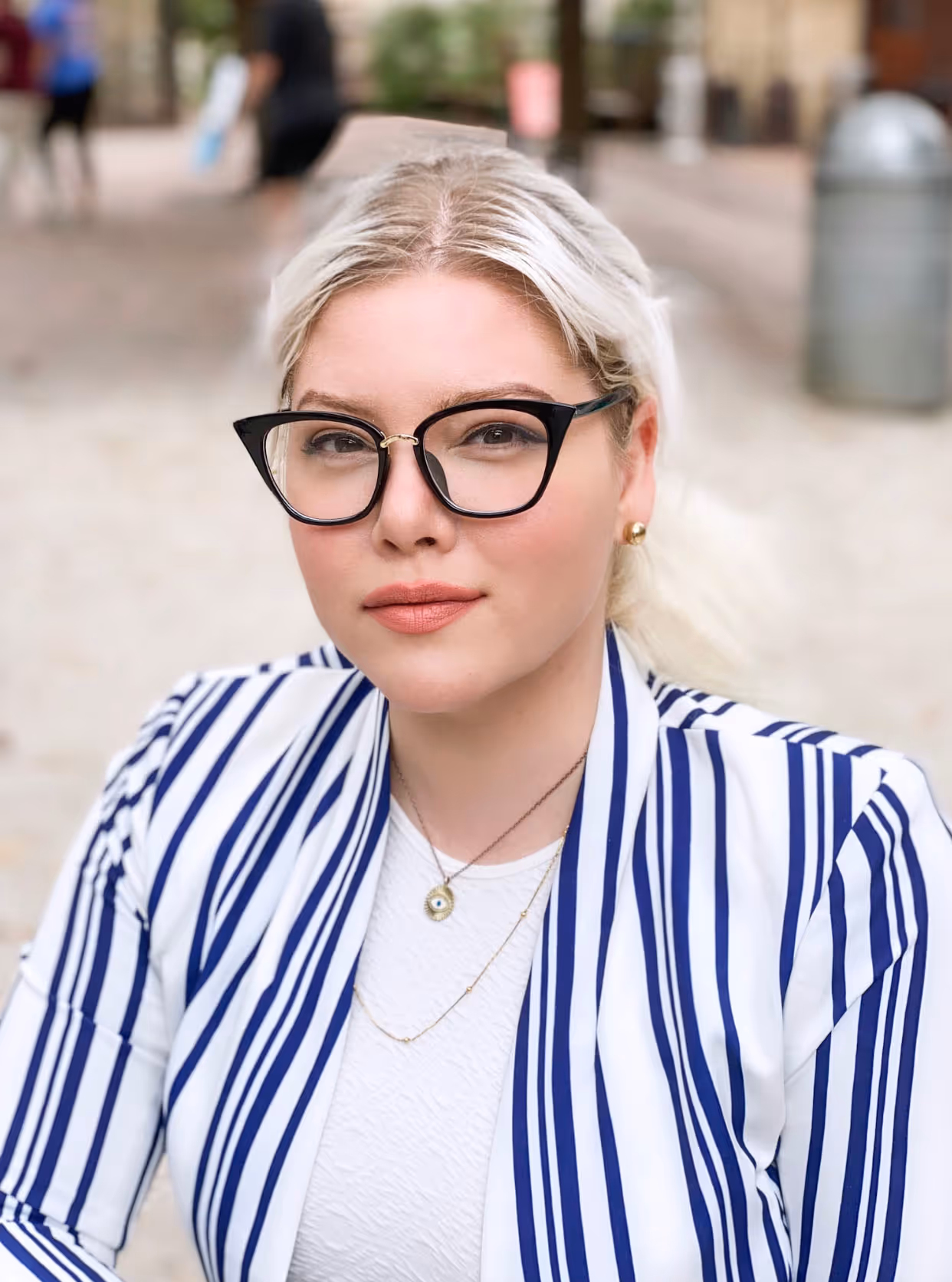 A portrait of Kathleen. She is wearing subtle makeup, glasses, and white and blue outfit.