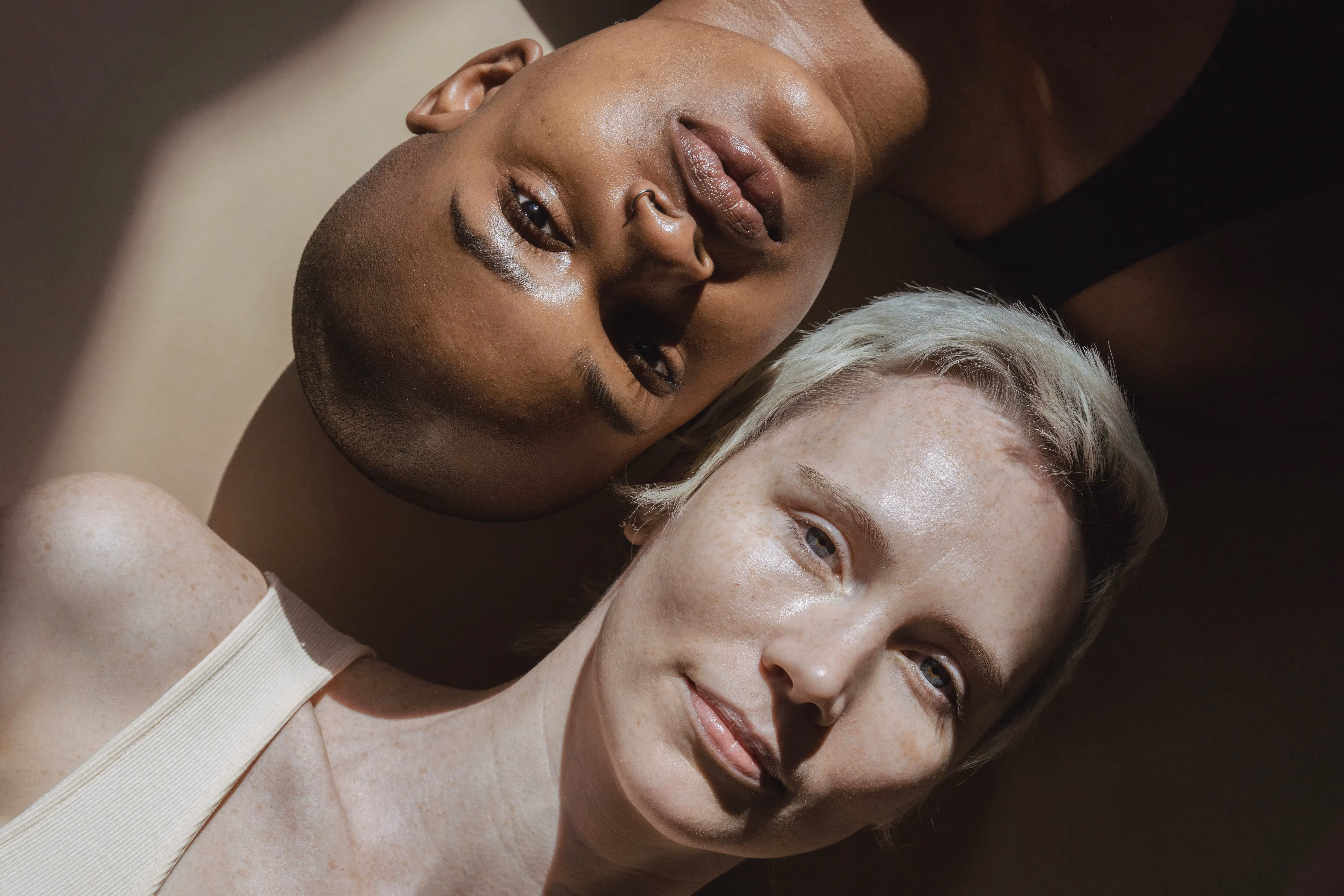 Photo of a POC laying to the right of a white person. They are looking directly at the camera.