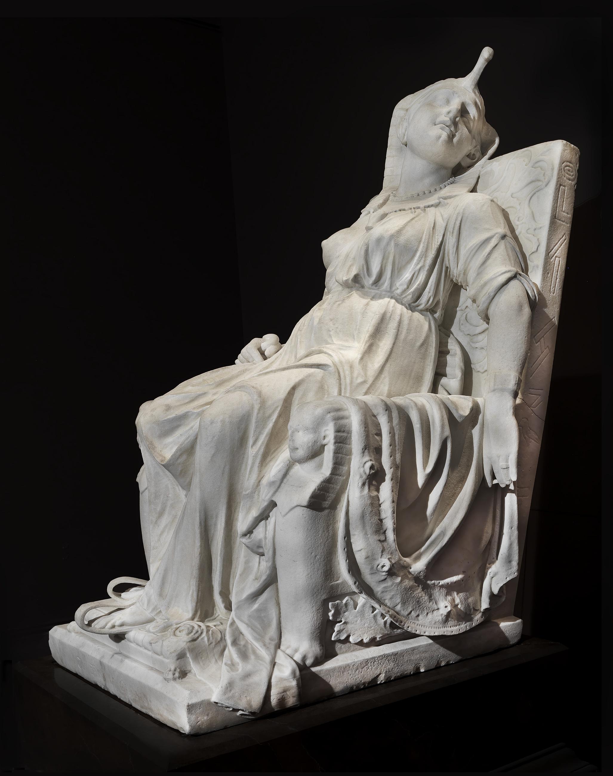 White marble sculpture by Edmonia Lewis of Cleopatra slumped on a throne after her death, her head tilted back and her arm hanging at her side.