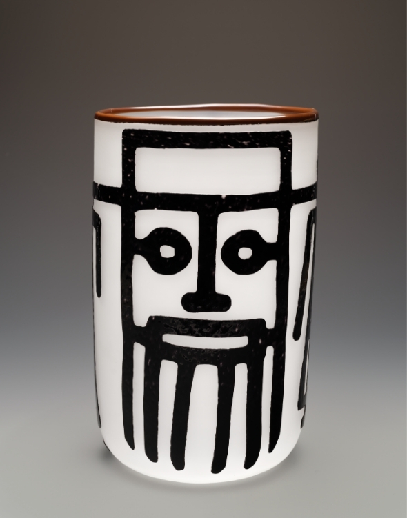 A white cylindrical glass vessel with bold black lines forming a simple face, with square eyes, a small nose, and vertical lines like a beard.