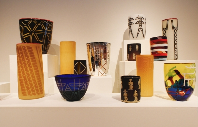 Baskets and glass vessels of different heights on white pedestals, many patterned in black-and-white geometric designs, alongside a yellow cylinder and a blue bowl.