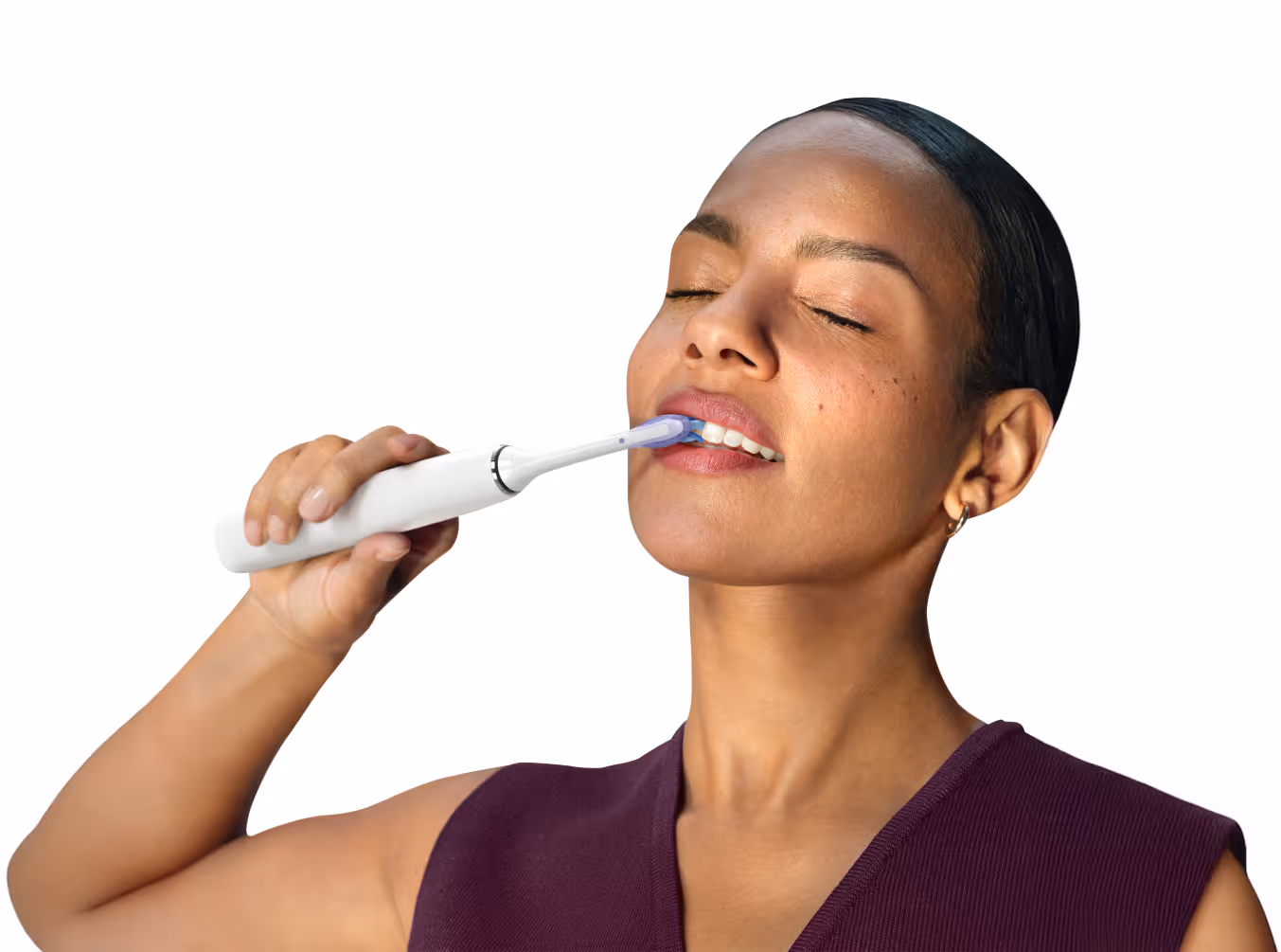 Woman with closed eyes using a white electric toothbrush on her upper teeth.