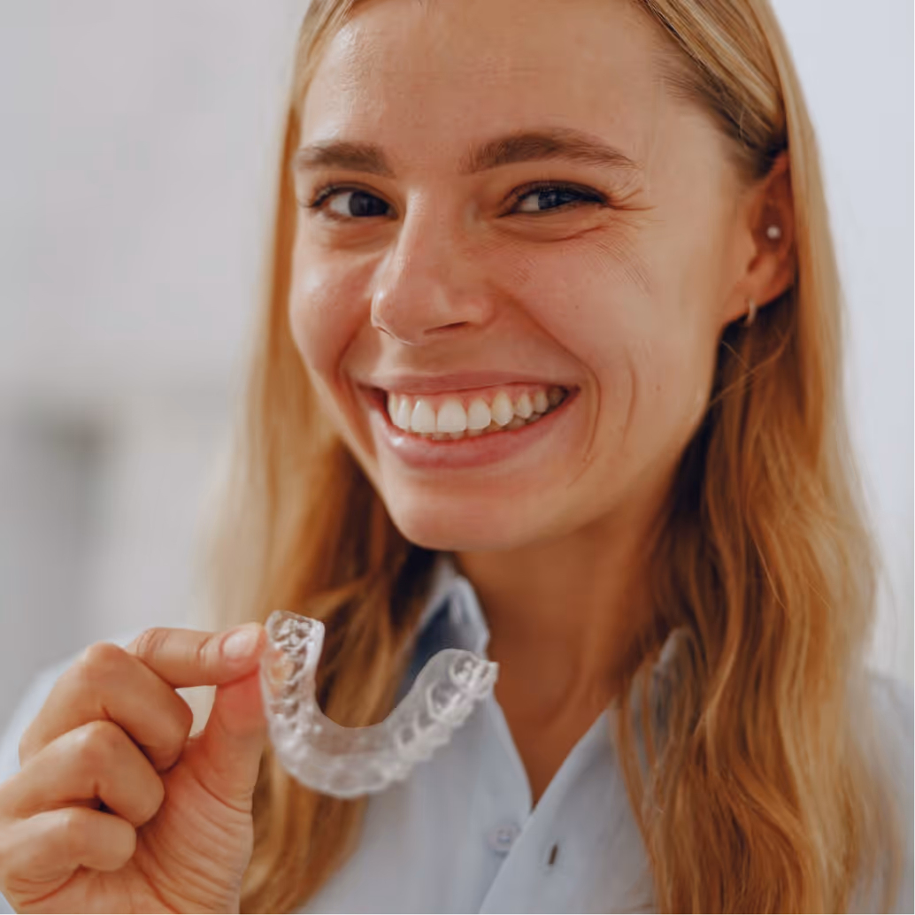 Smiling woman holding a clear dental aligner in her hand.