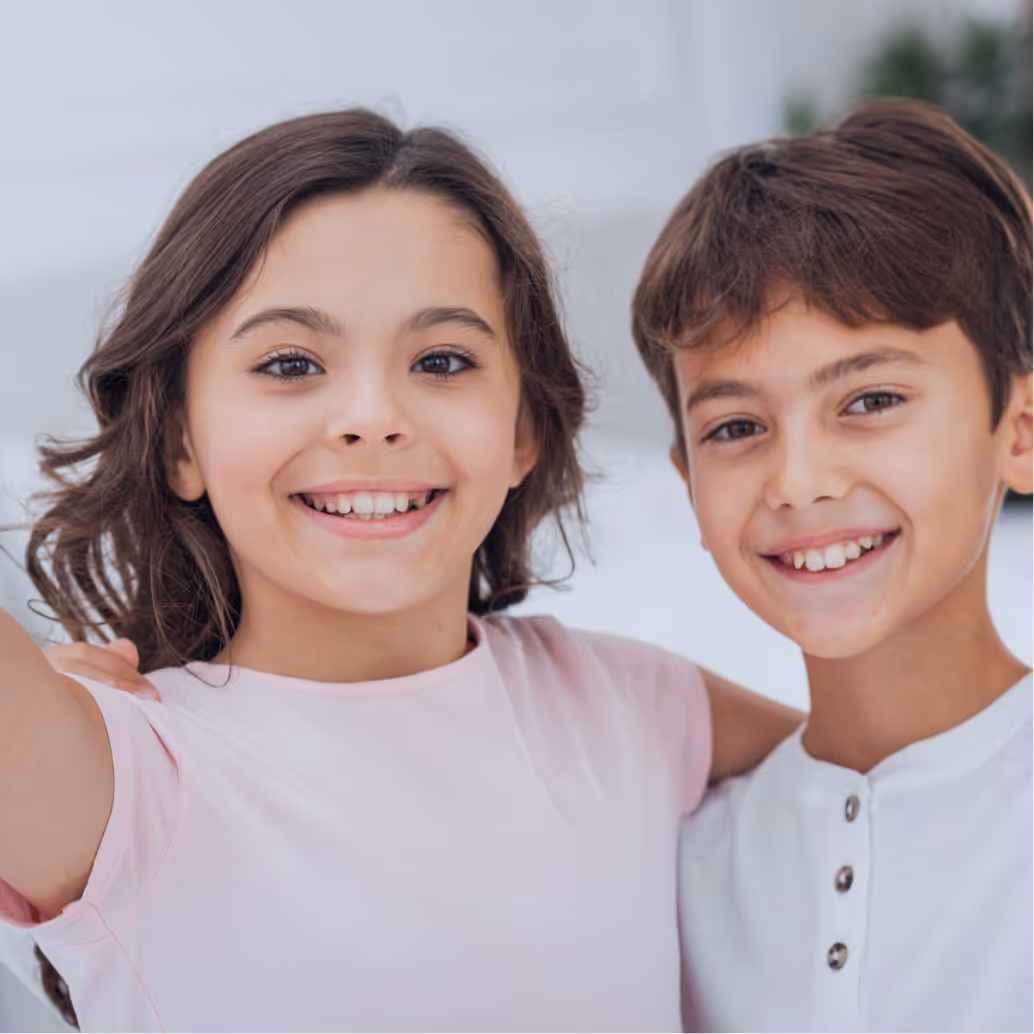 Smiling young girl and boy with brown hair posing closely together indoors.