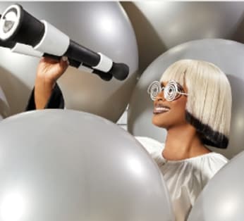 Person looking through a telescope surrounded by silver balloons