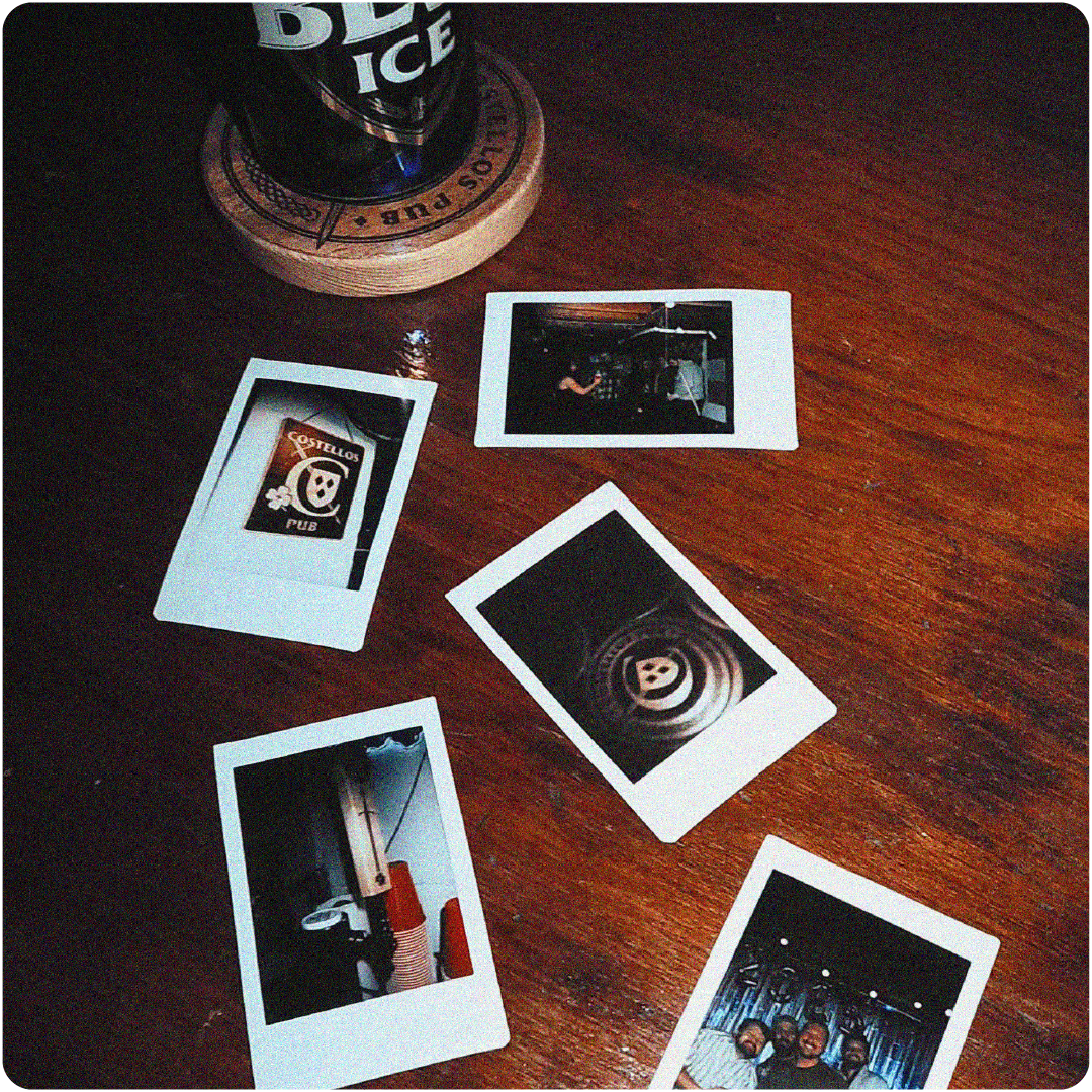 Wooden table with five Polaroid photos scattered around a glass on a coaster.