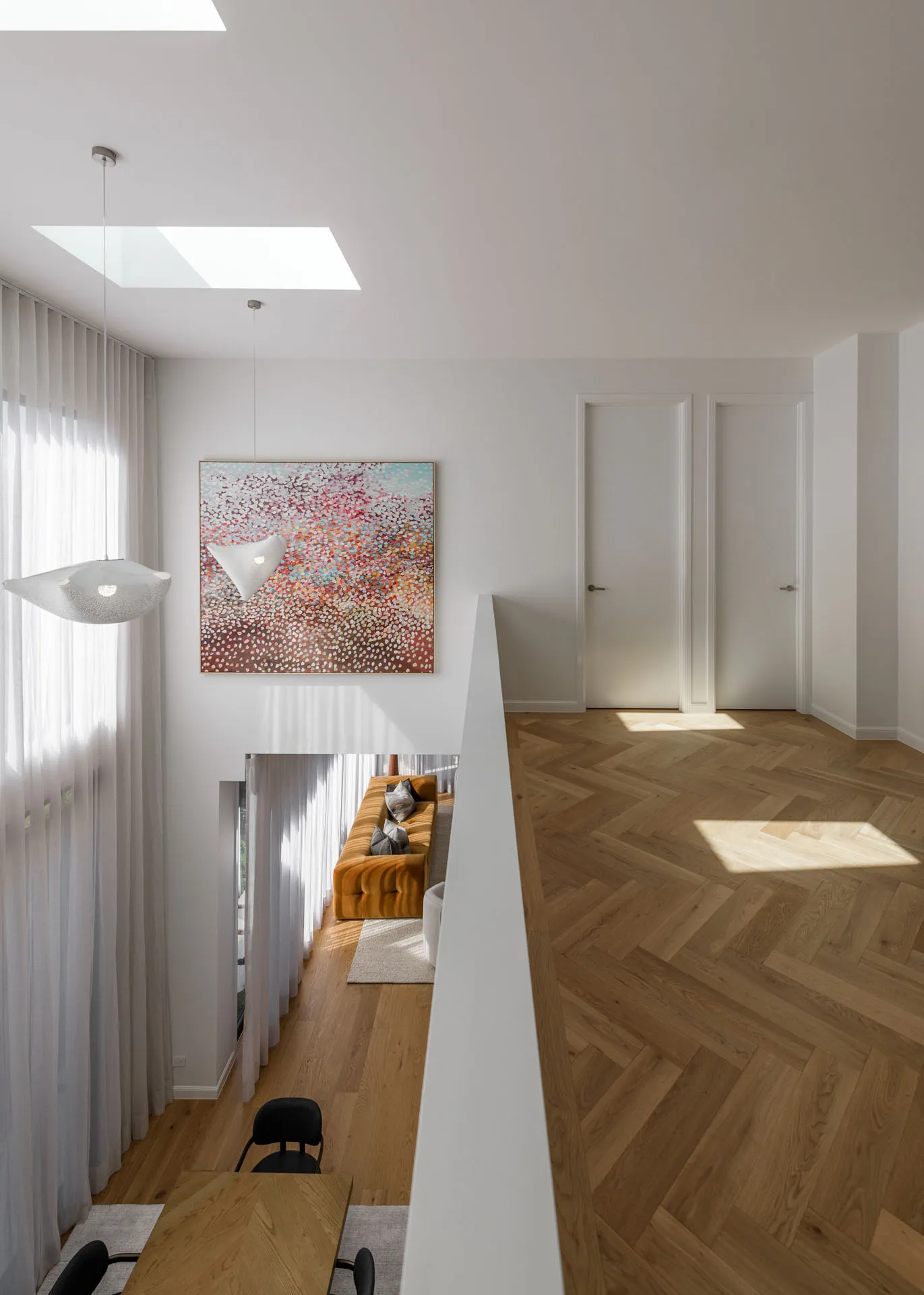 Bright modern living space with wood floors, mustard sofa, large abstract art, and two white doors upstairs.