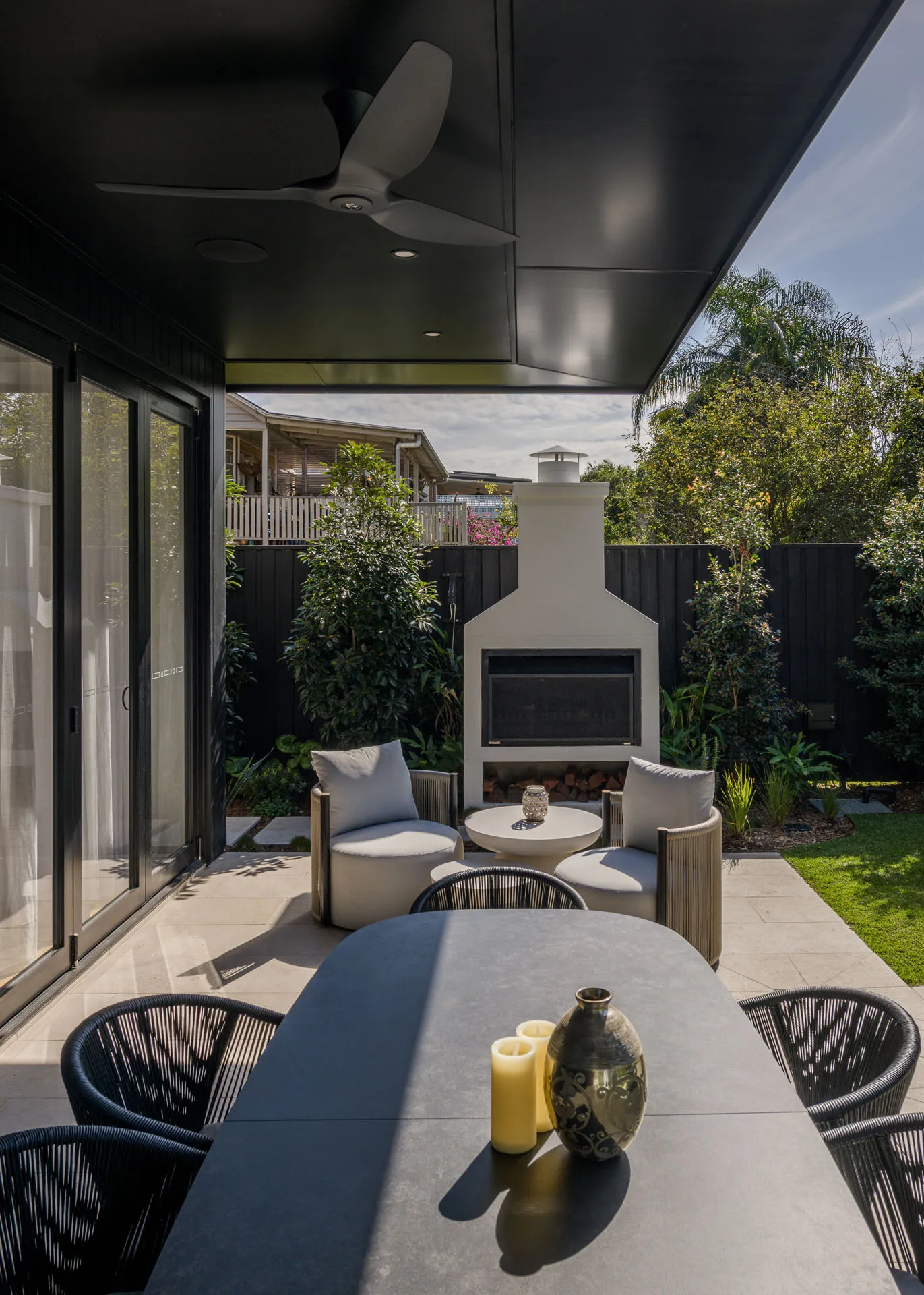 Modern patio with a dark table, chairs, two cushioned seats, and a white outdoor fireplace.