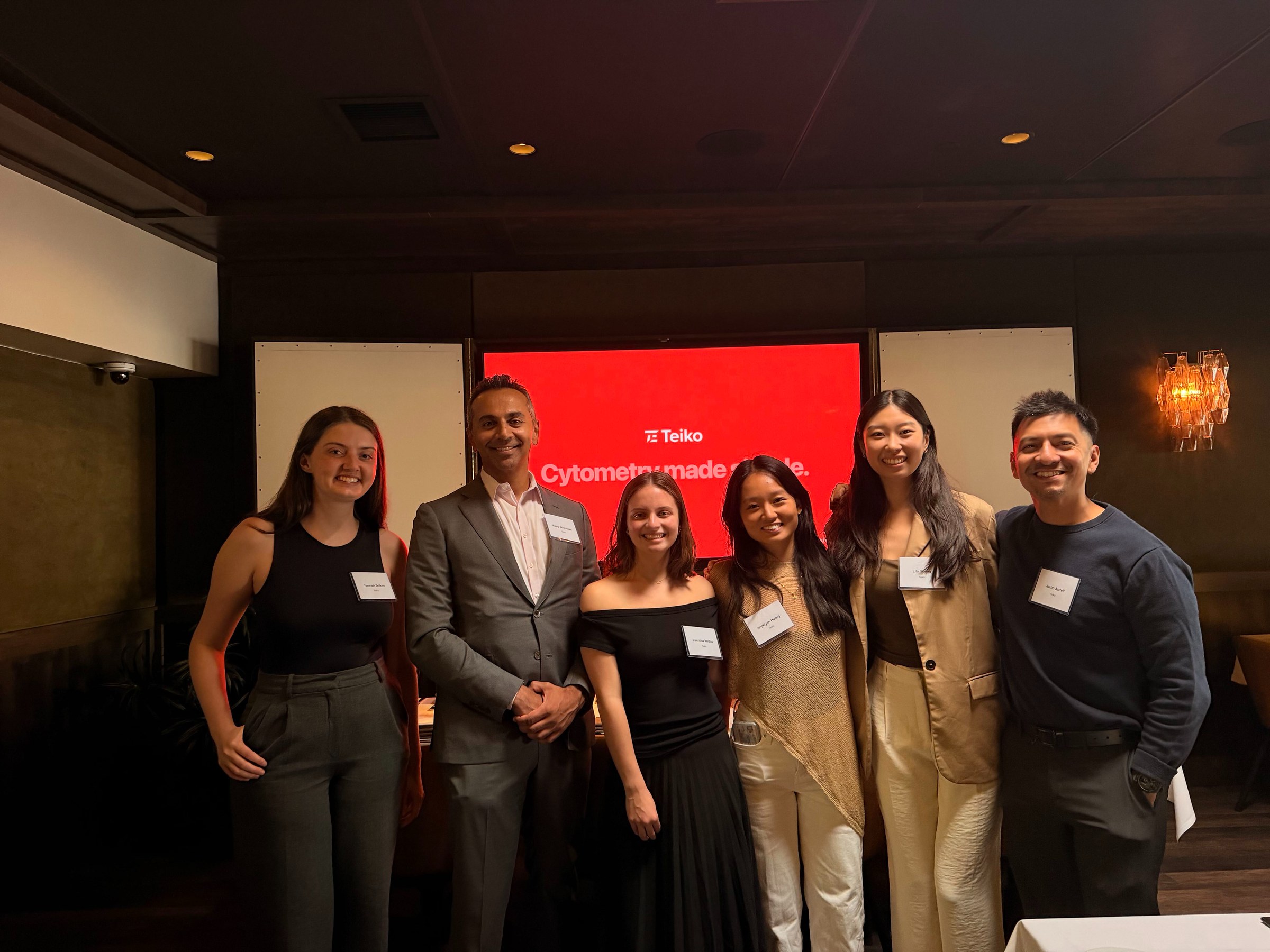 Six Teiko teammates at an event in front of a red Teiko screen