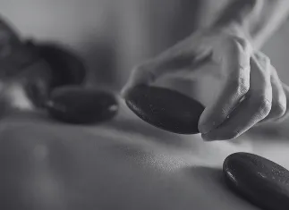 Close-up of a hand placing a smooth hot stone on a person's back during a massage.