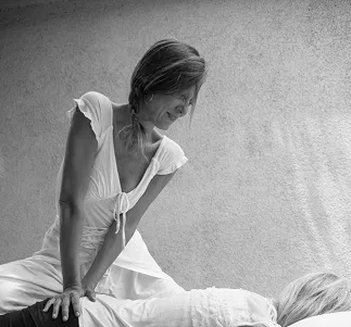 Woman in white dress giving a massage or therapeutic bodywork to a person lying down.
