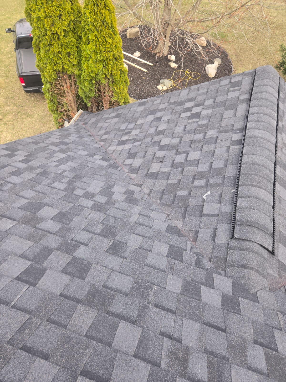 Gray architectural shingle roof with a ridge vent and trees nearby