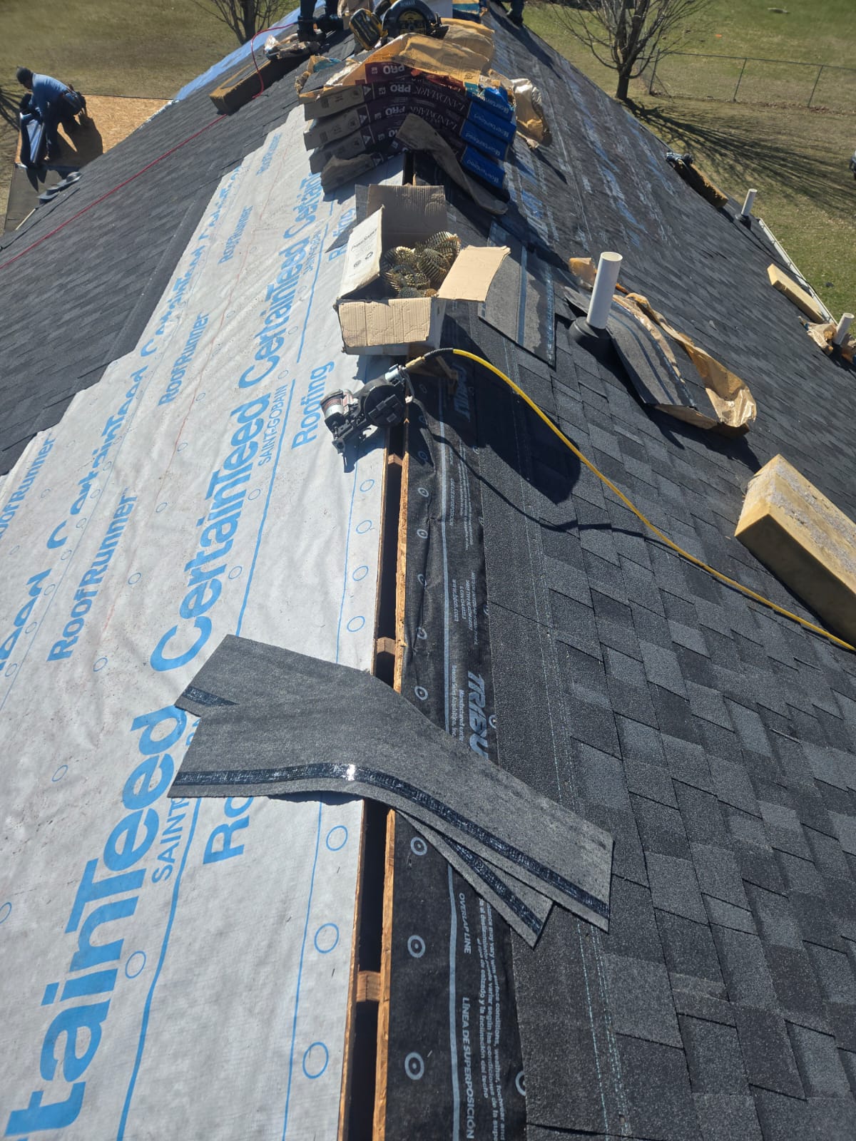 Roof being re-shingled over blue underlayment with tools on the roof deck
