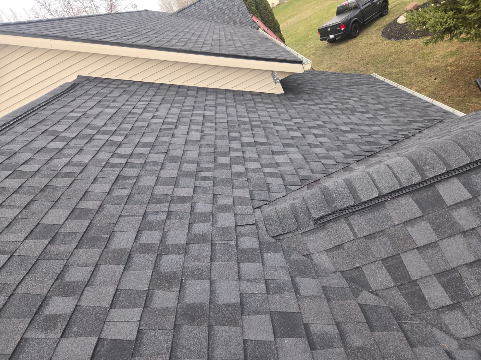 Dark gray asphalt shingle roof with a hip and ridge cap beside a tan house