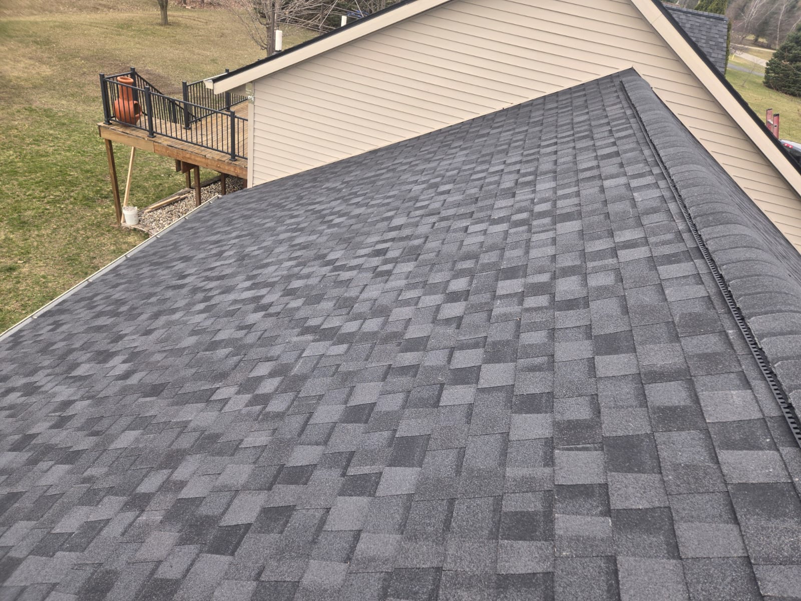 Gray asphalt shingle roof with a ridge cap on a house with a deck