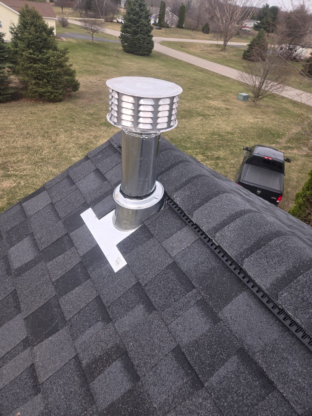 Gray shingle roof around a metal vent pipe with flashing