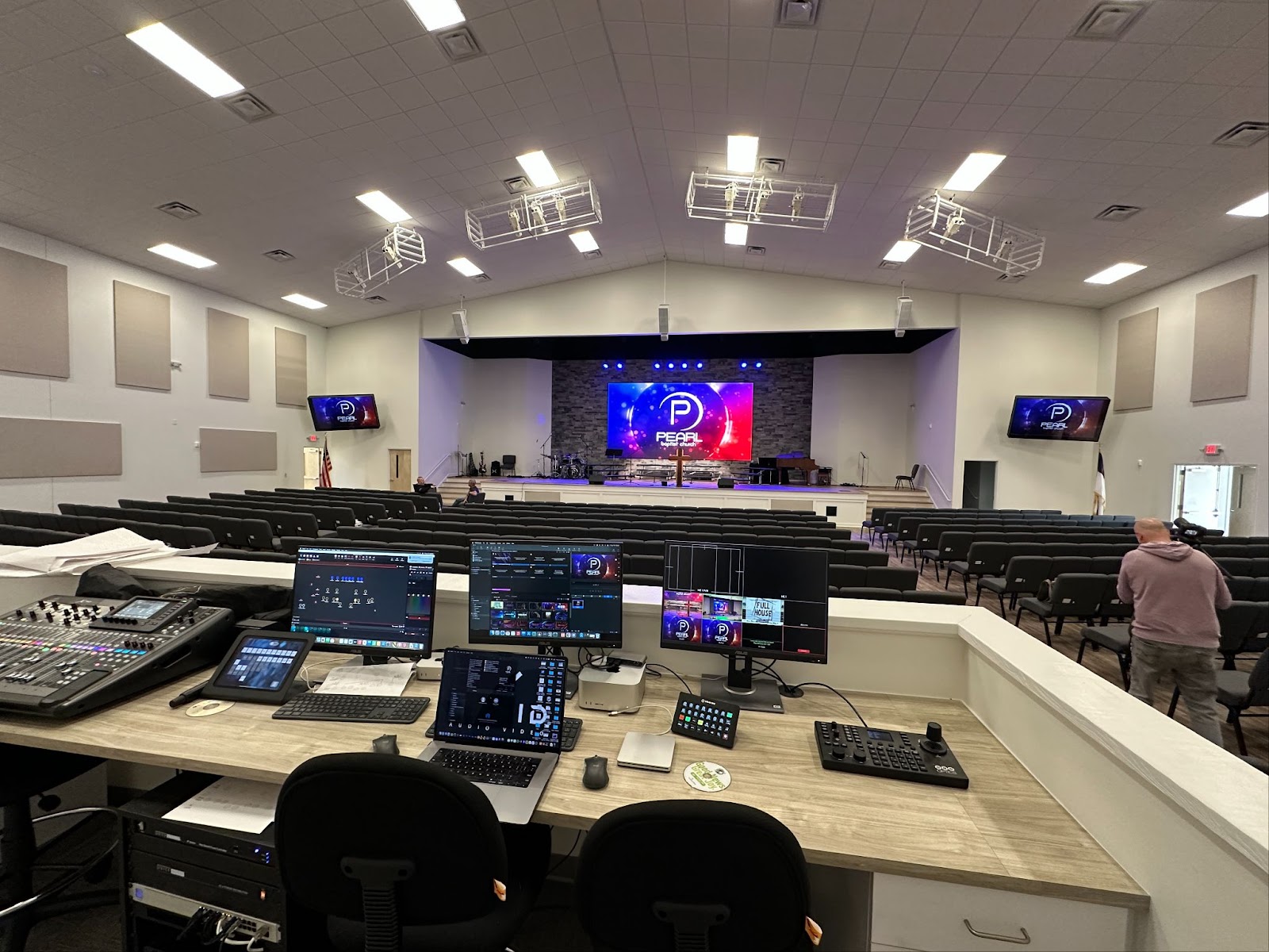 Professional AV control station in church sanctuary showing multiple monitors, mixing board, and control systems managing stage lighting, audio, and video displays