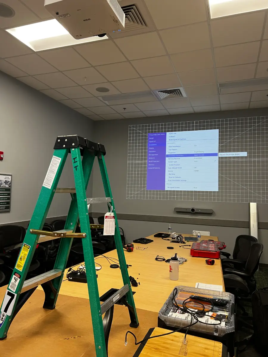 AV technician on ladder performing system maintenance and calibration in corporate conference room