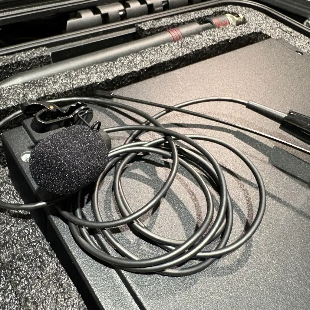 Close-up of lavalier microphone capsule with foam windscreen and cable showing proper placement setup