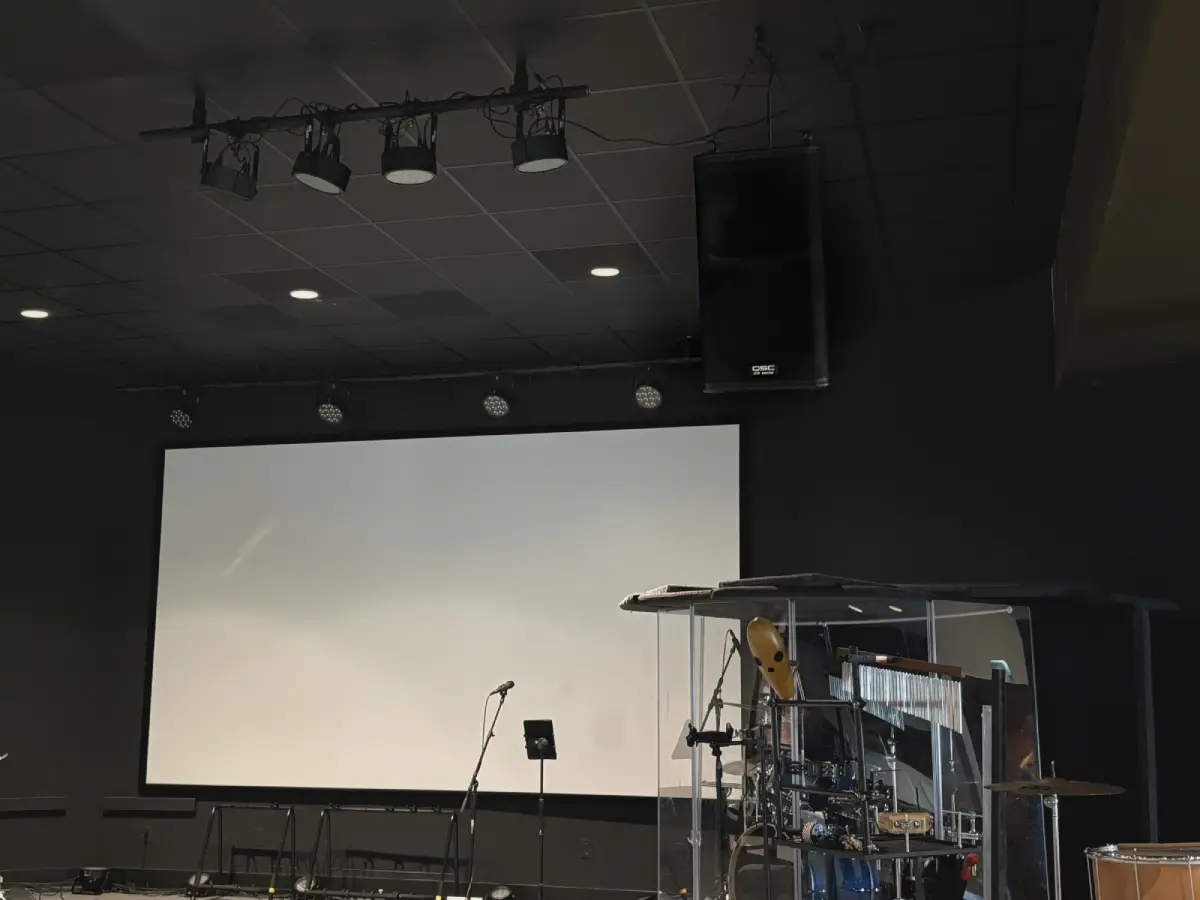 Small church stage setup with keyboard, drum kit, microphone stands, and professional speaker system