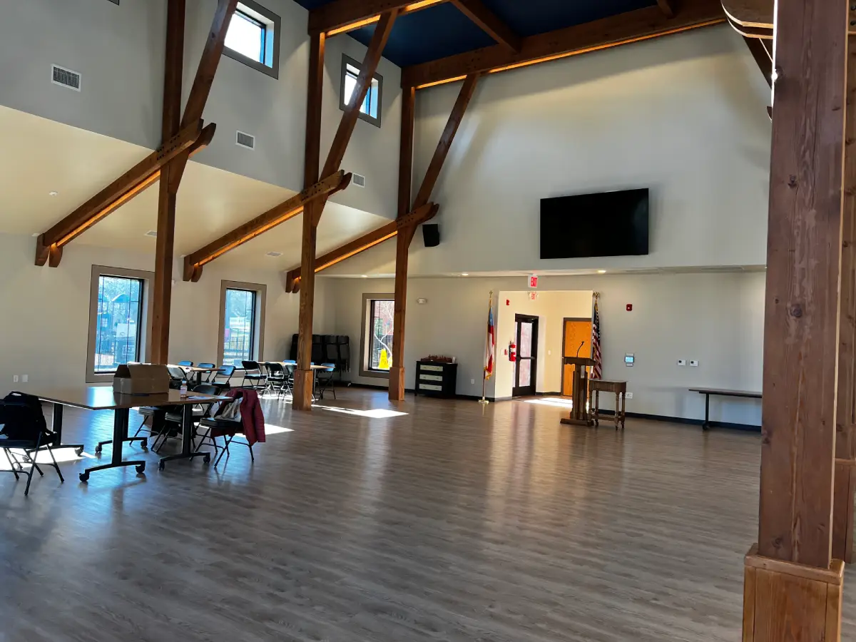 Open church fellowship hall with high ceilings, hardwood floors, and exposed timber frame beams showing reflective surfaces that contribute to poor room acoustics