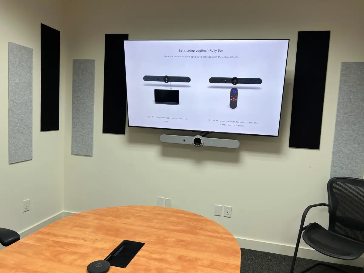 Wall-mounted commercial display with video bar installed in a small conference room with acoustic panels