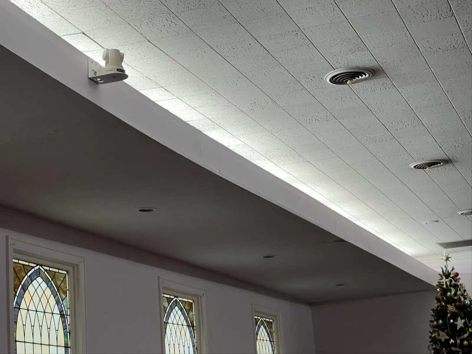 PTZ camera mounted on rear wall of church sanctuary with stained glass windows below
