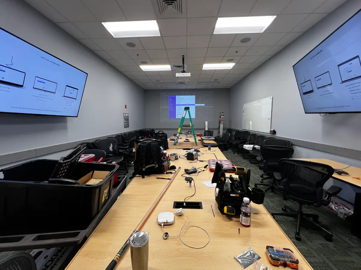 Conference room AV installation in progress with dual wall-mounted displays, ceiling projector, and tools staged on the conference table