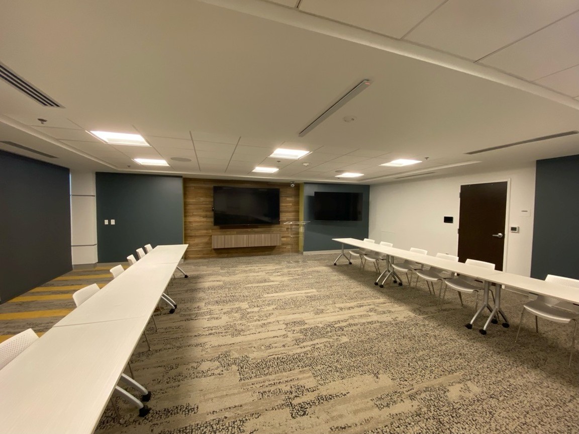 Boardroom-style conference room with rectangular table, wall-mounted display, and video bar