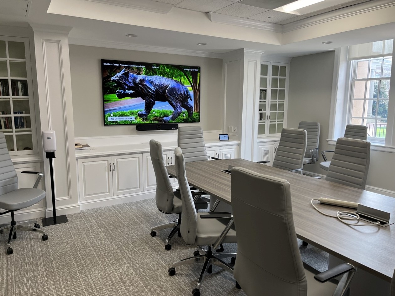 Classroom-style conference room with rows of tables facing two wall-mounted displays