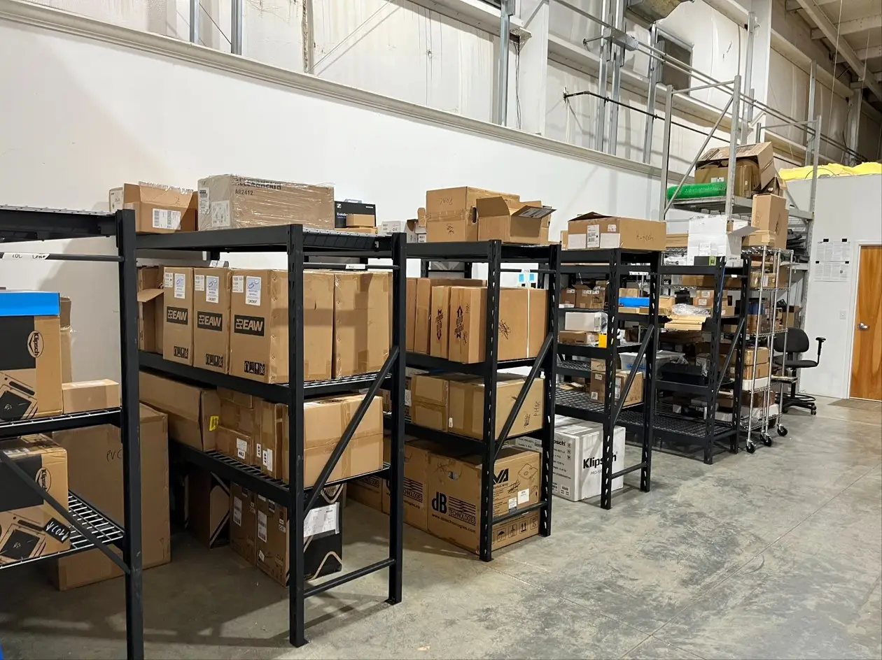 Boxed AV equipment on warehouse shelving awaiting installation