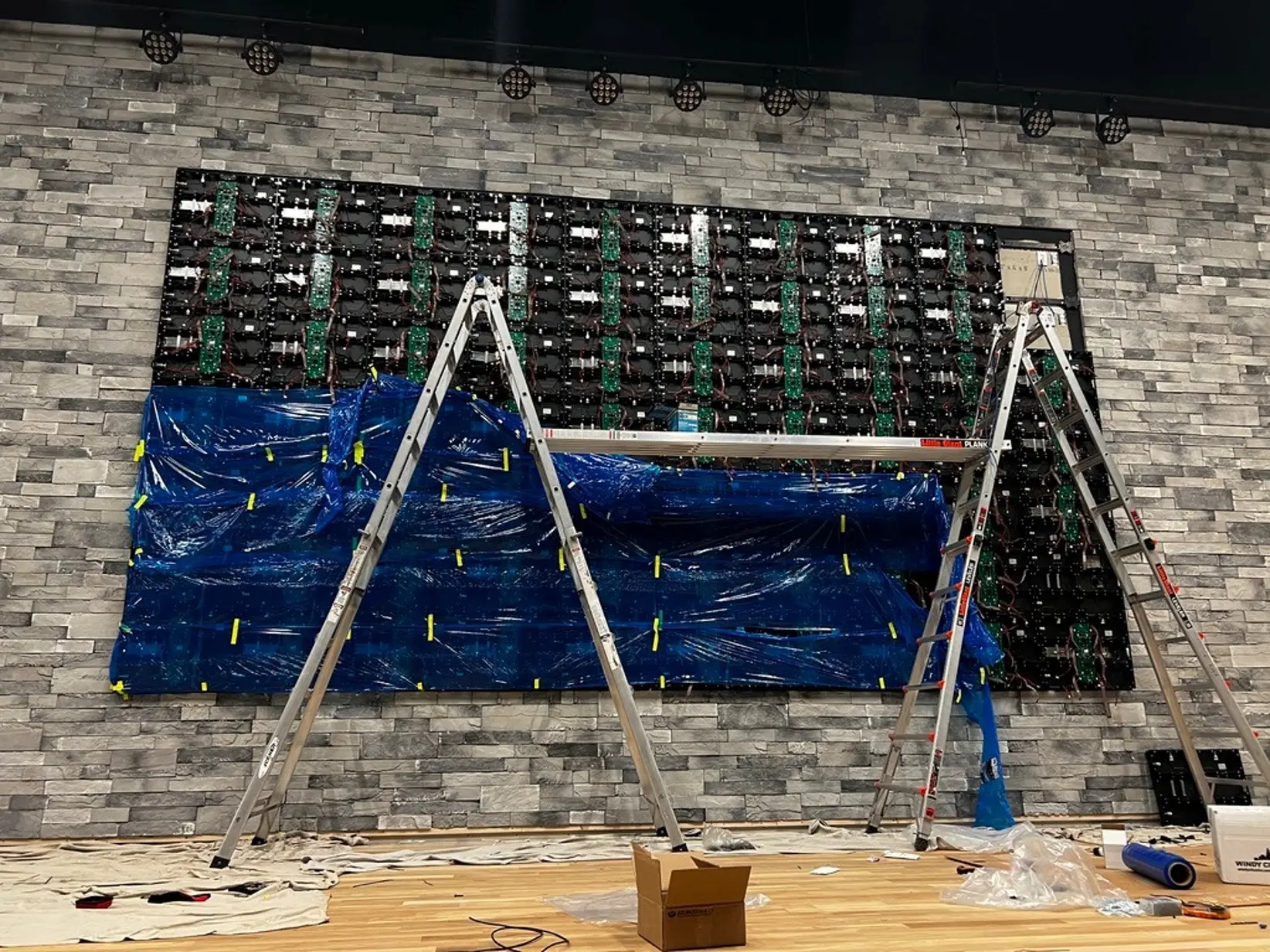 LED video wall cabinets mounted on a stone wall, lower panels wrapped in protective plastic mid-install