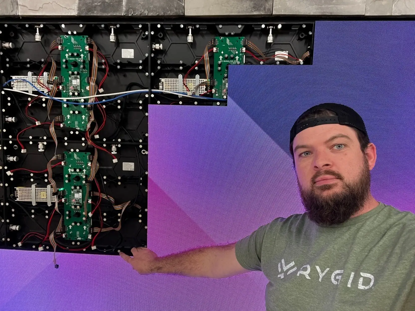 Ryan of RYGID AV pointing to the power supplies and control boards behind an open LED wall section