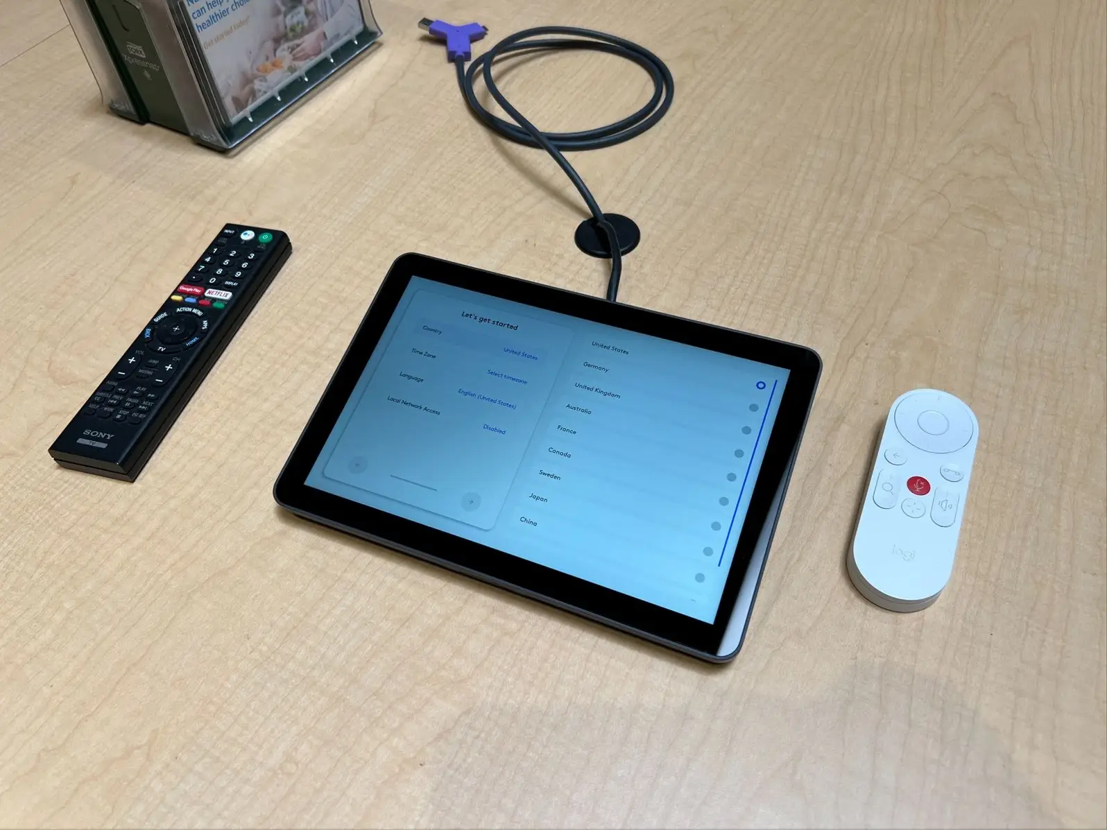 Conference room touch controller on a table beside a laptop connection cable and two remotes