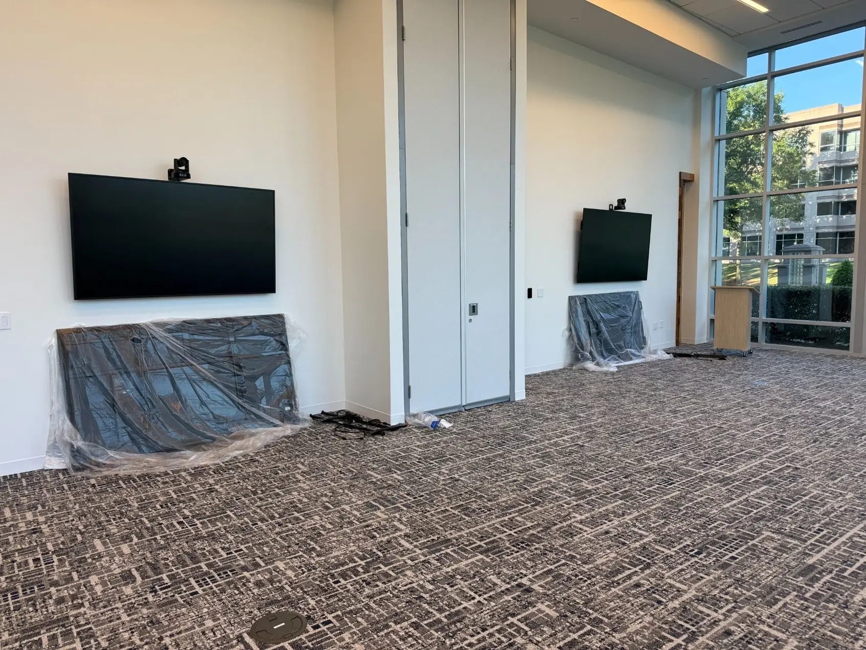 Large meeting space with two wall displays and PTZ cameras, a high ceiling and a floor-to-ceiling glass wall