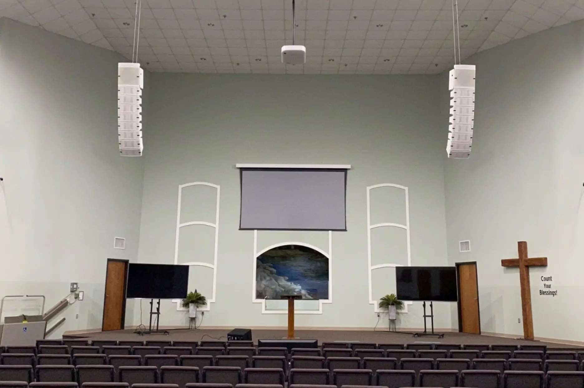 Church sanctuary with two line array speakers hung above the stage and a projection screen