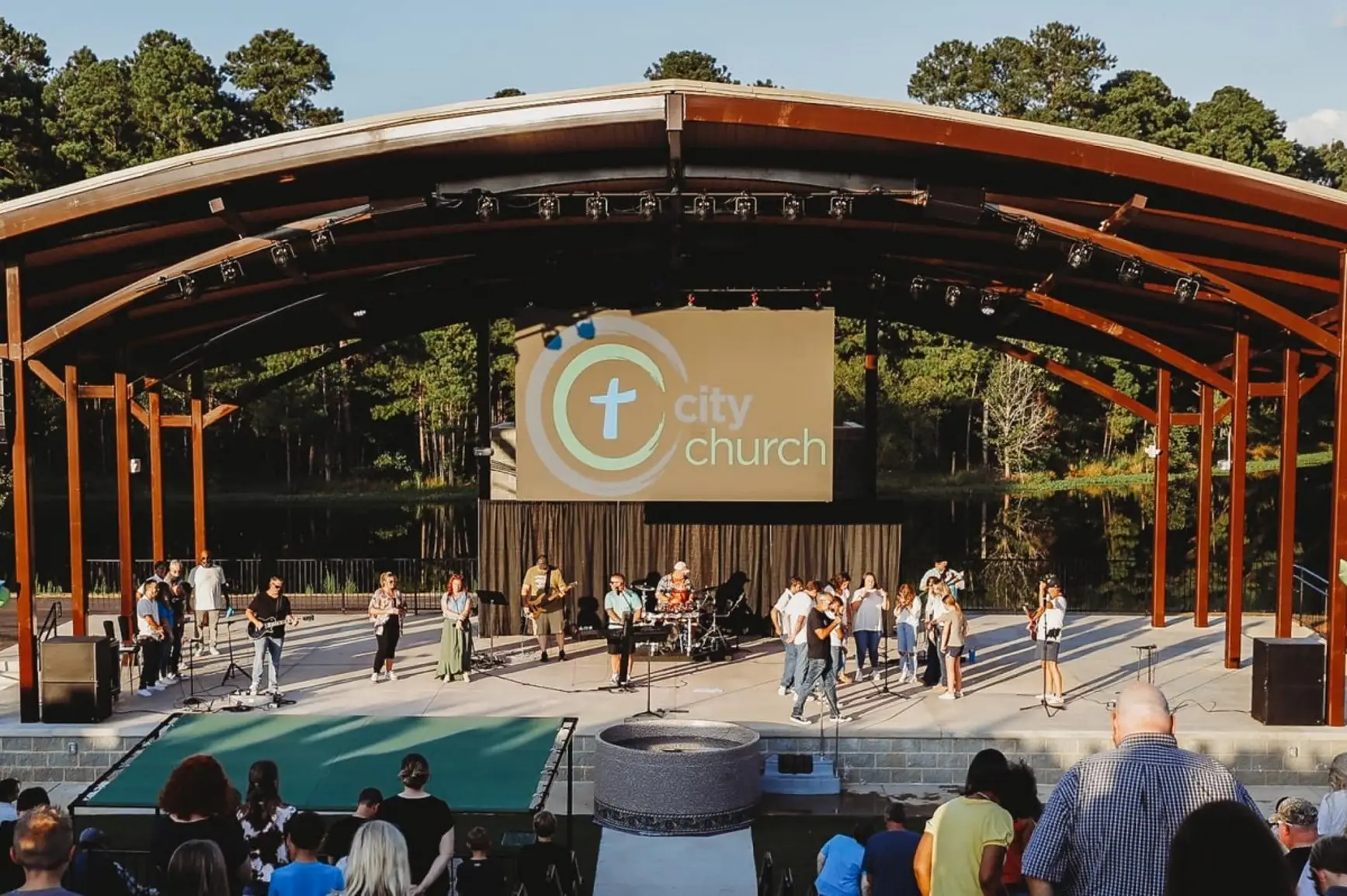 Worship band performing on an outdoor amphitheater stage as the congregation stands