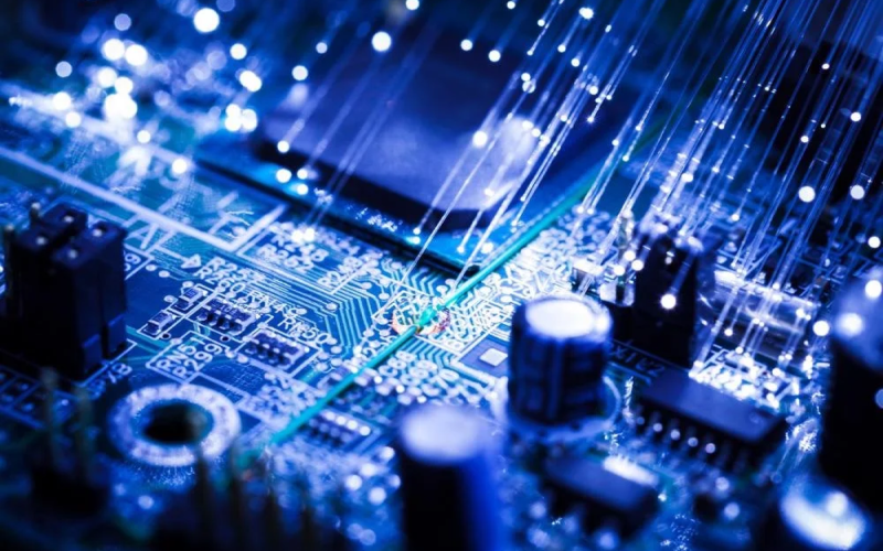 Close-up of a blue circuit board with glowing fiber optic strands and electronic components.