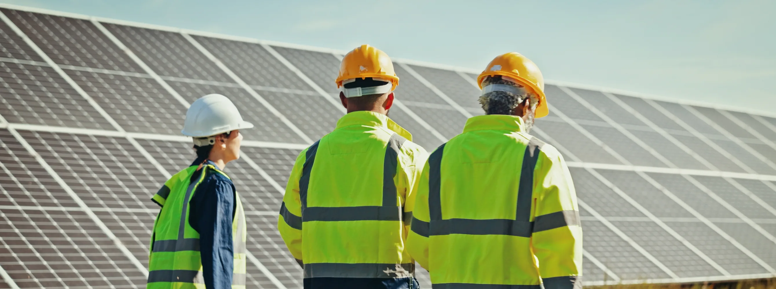 Asiantuntijat kävelevät suurien aurinkopaneelien edessä kypärät päässä