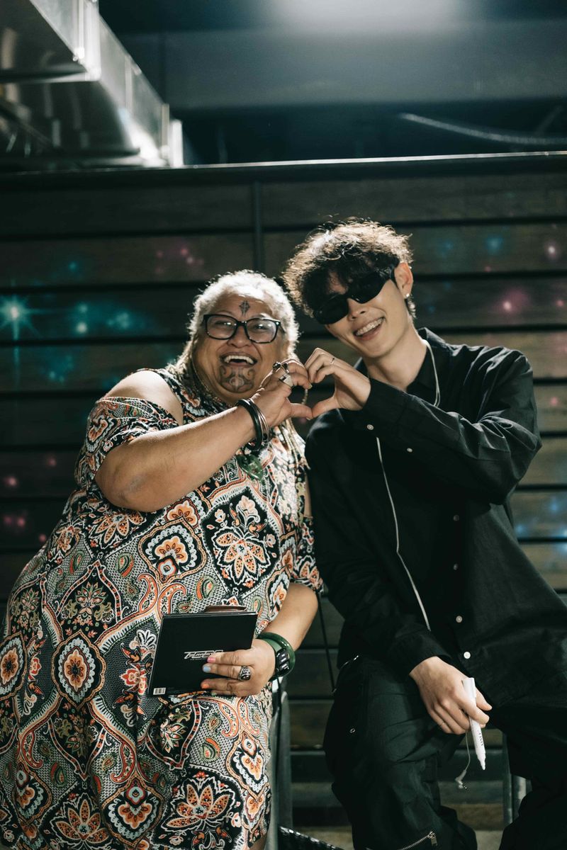 Jimmy Brown in sunglasses making a heart sign with a smiling woman in a patterned dress backstage