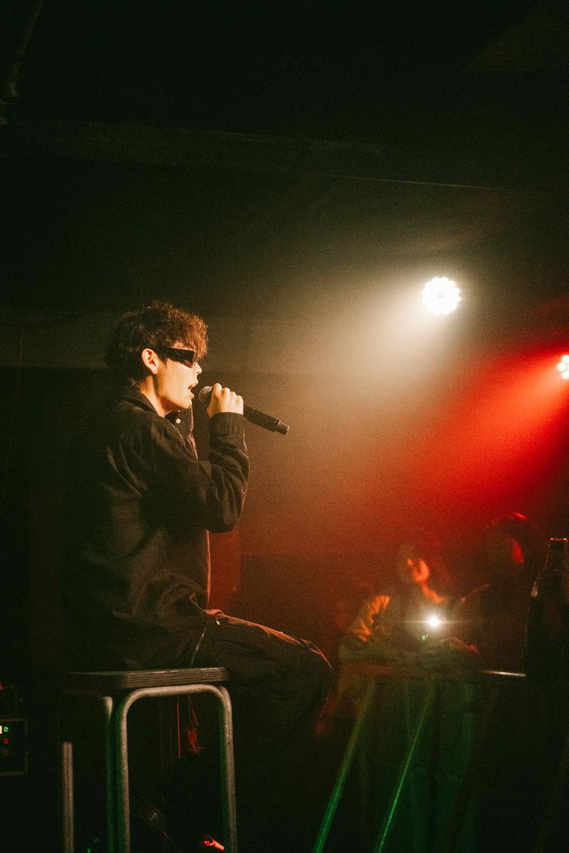 Jimmy Brown seated on a stool singing in sunglasses with fans watching under red and white lights