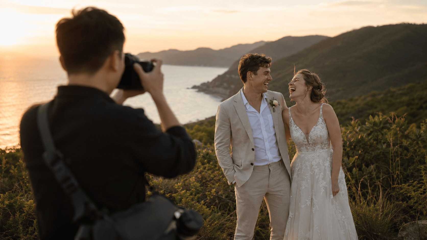 Wedding photographer capturing a candid, unposed moment of a laughing bride and groom on a coastal hillside at sunset, documentary-style Auckland wedding photography by Vantirra