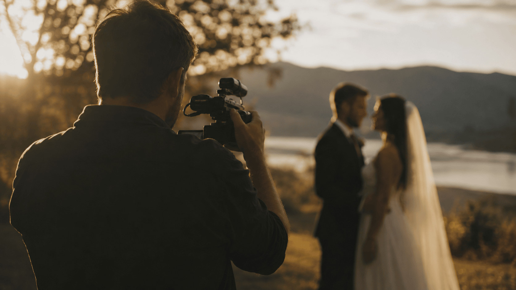 A wedding videographer filming a couple during golden hour, capturing footage for their highlight film