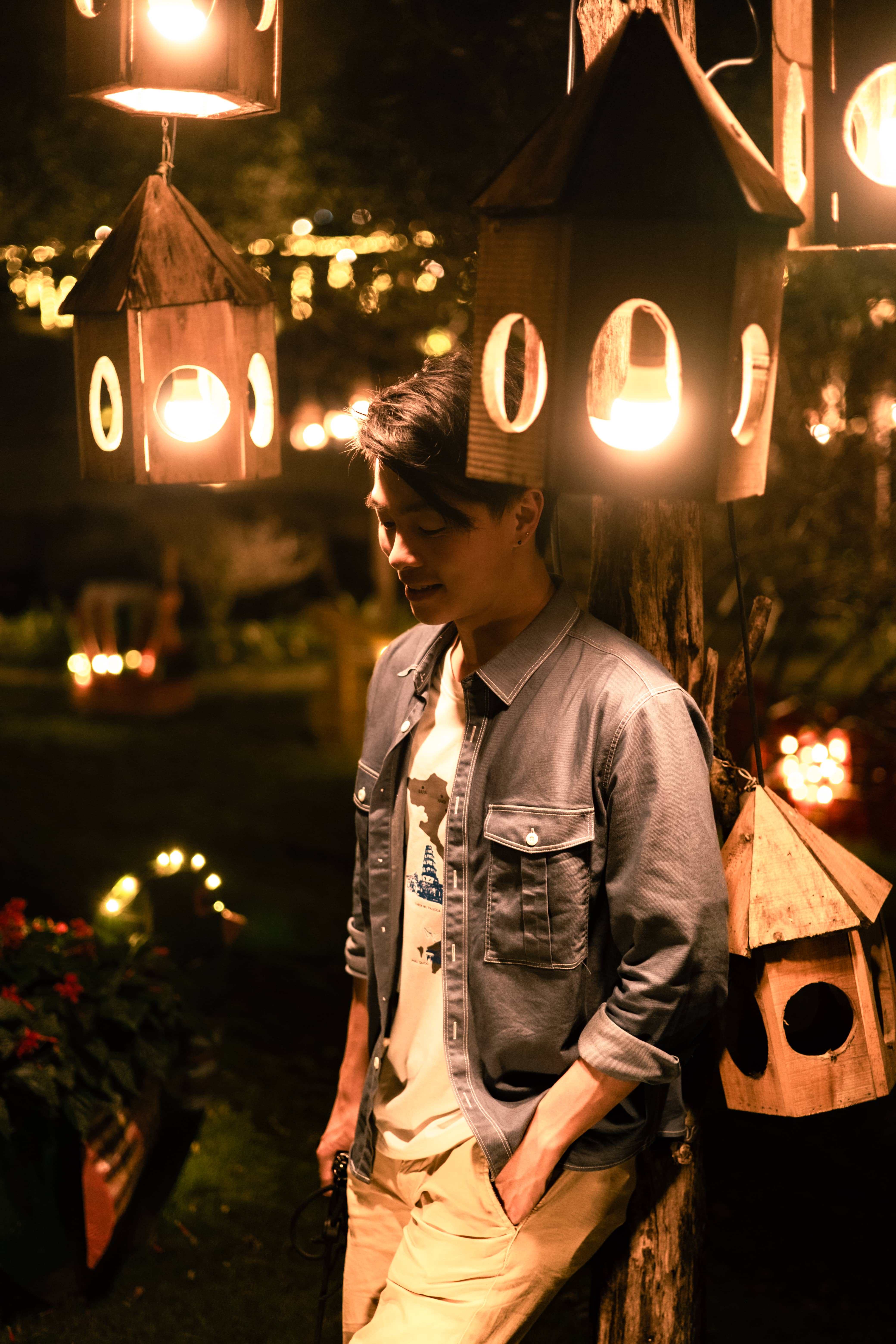 Man in a denim jacket beneath glowing wooden lanterns at night, Vietnam