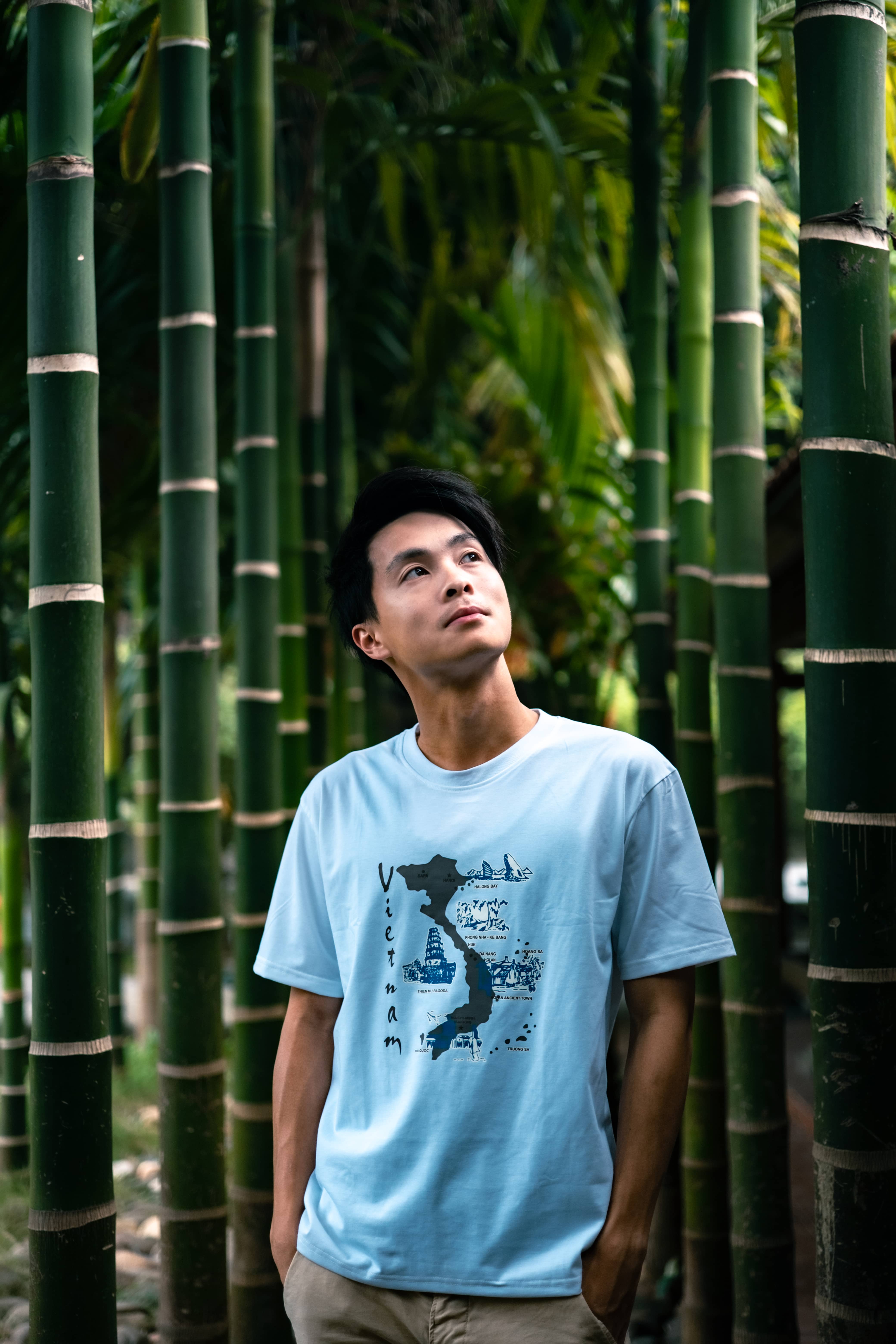 Man in a light blue Vietnam map t-shirt standing among tall green bamboo stems, looking up