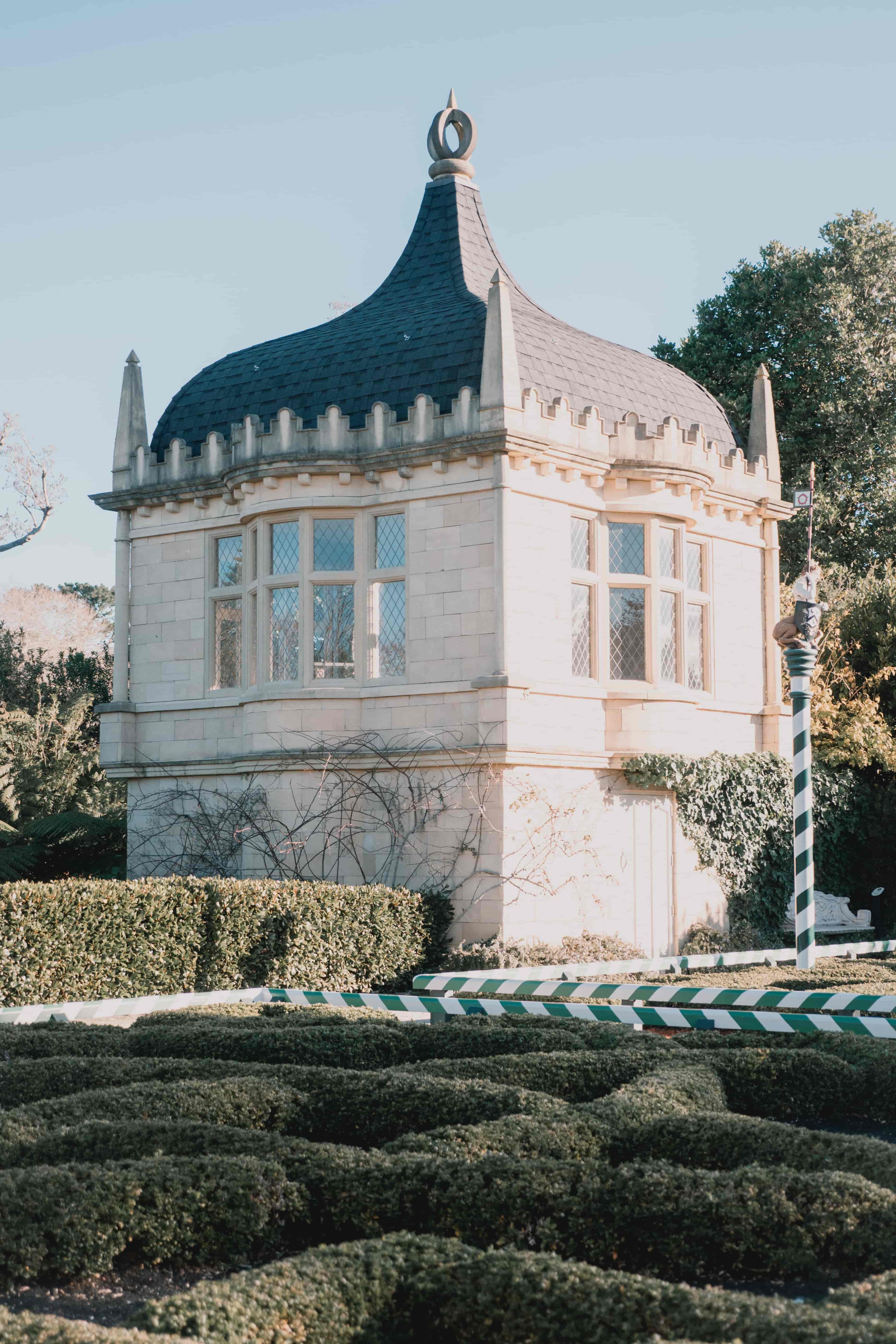 Ornate white pavilion with a dark curved dome above low knot garden hedges in soft afternoon light