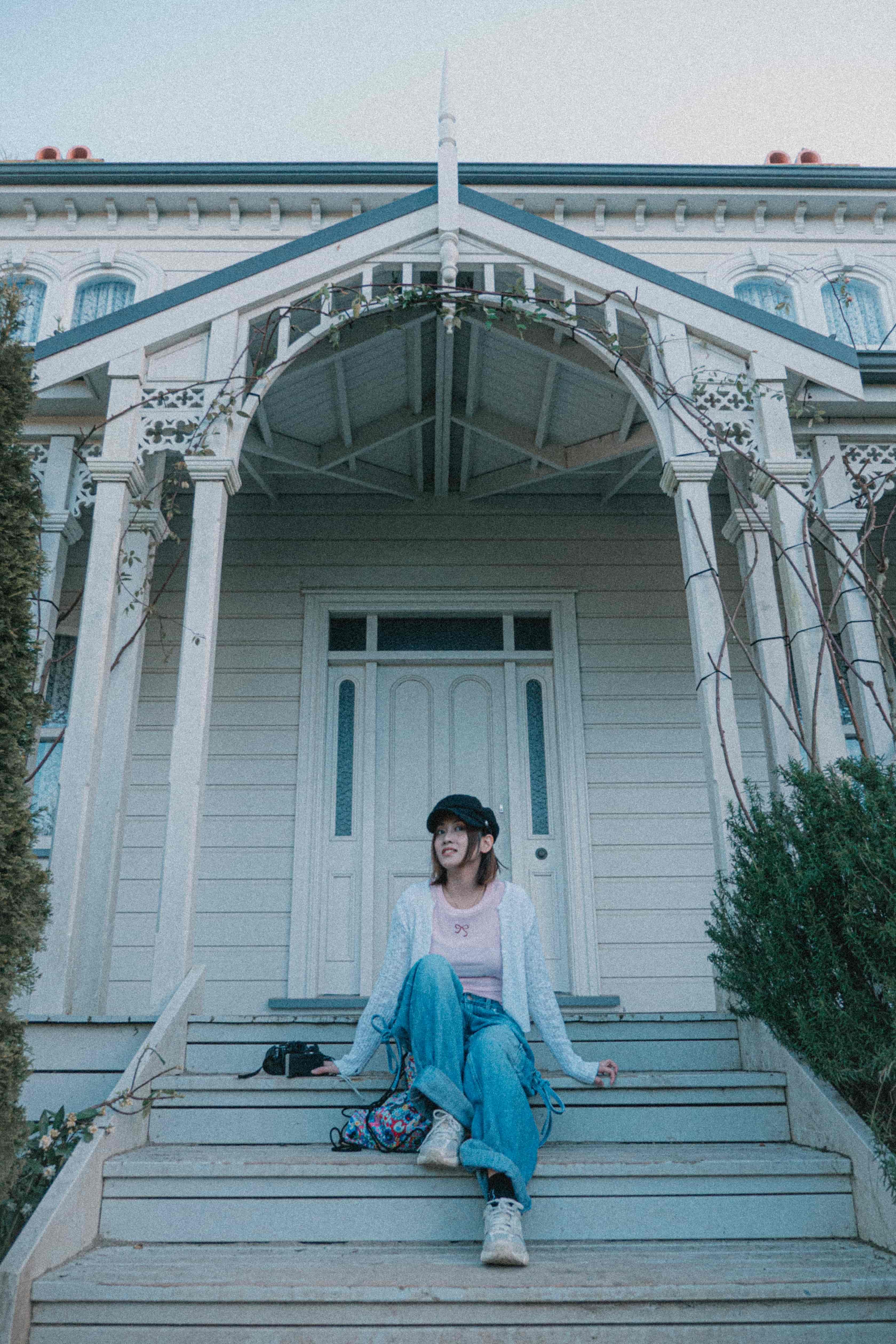 Woman sitting on the front steps of a white wooden villa with a carved arched porch